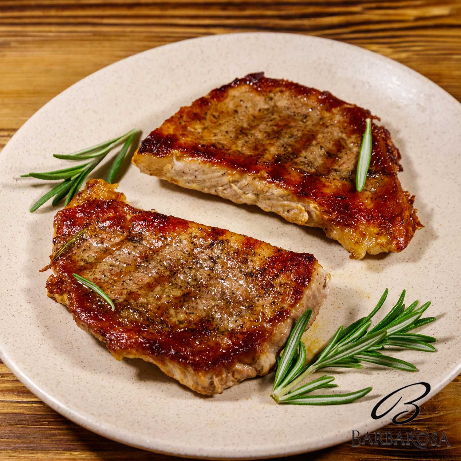 Grilled pork steaks with rosemary on wooden table